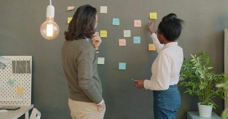Two colleagues reviewing sticky notes on an office wall during an organisational development workshop